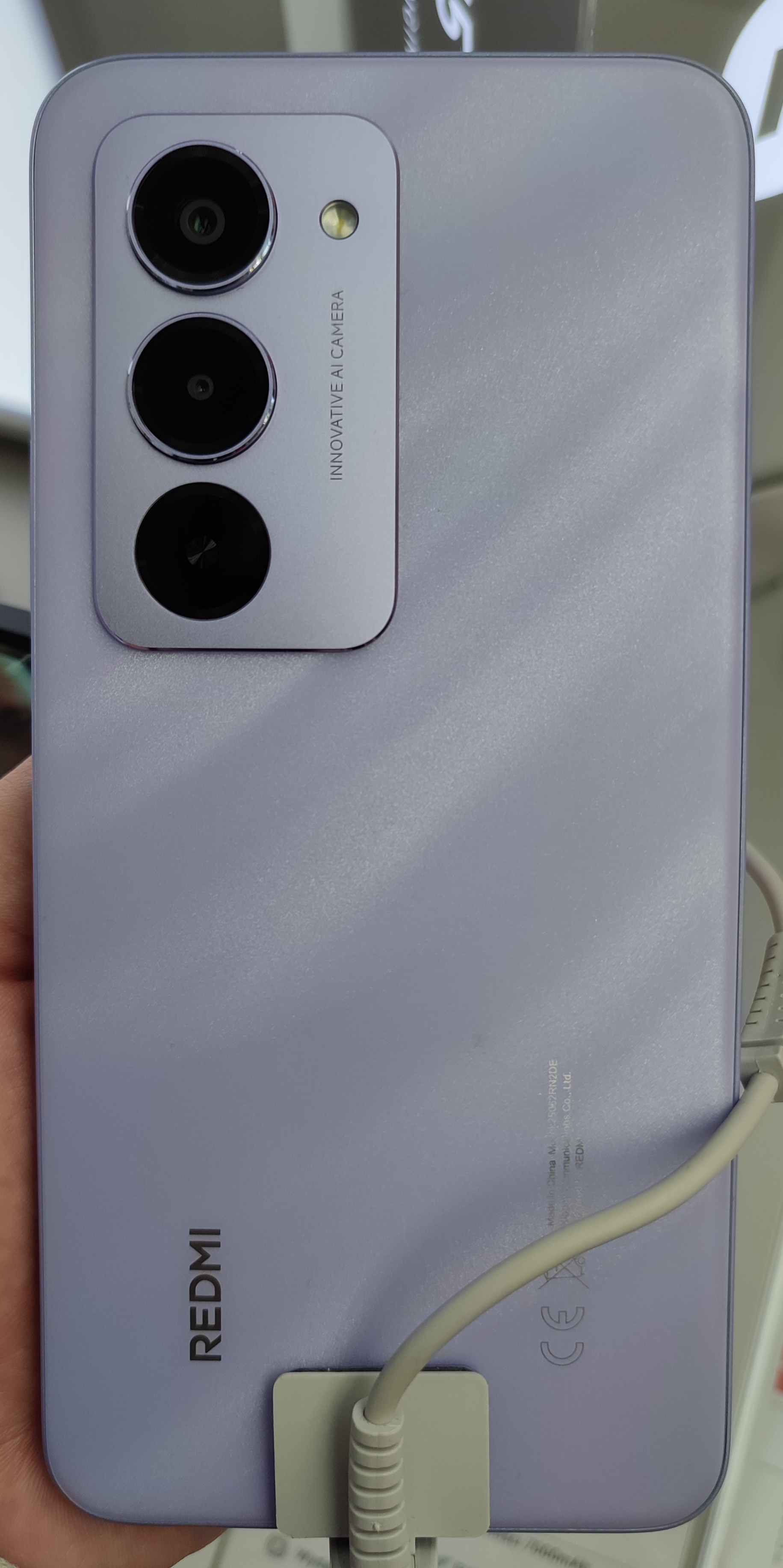 Rear of a Sandy Purple Redmi 15 held on a shop display
